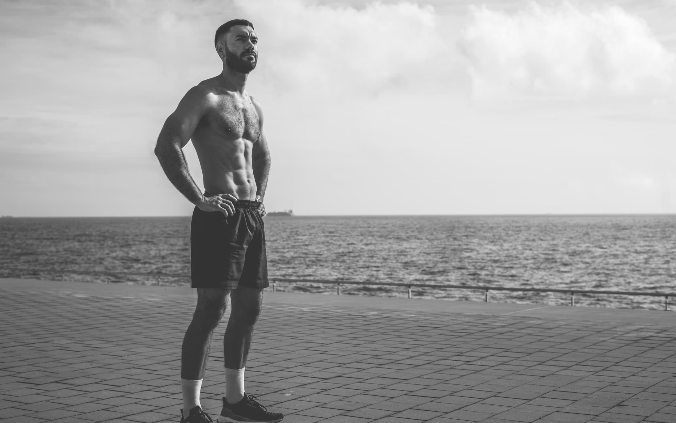 Athletic man standing by the sea, looking toward the horizon